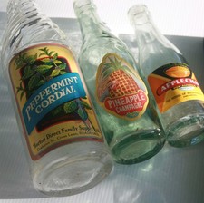 Trio of vintage soft drink bottles with colourful genuine old labels for display